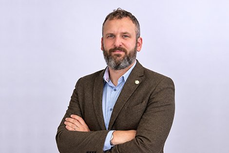 Headshot of Jon Ladd, Land & New Homes Network, smiling with arms folded in a brown tweed jacket and blue shirt
